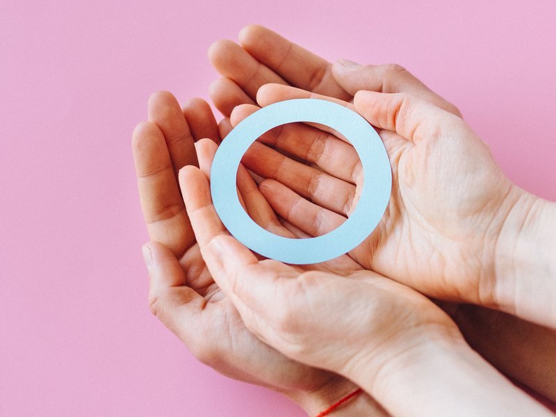 Cupped hands gently holding a light blue paper circle against a soft pink background