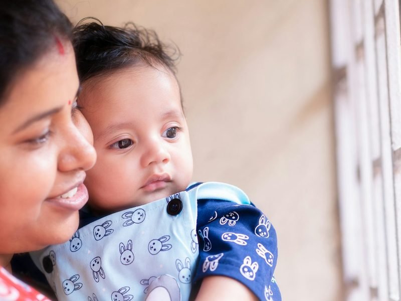 A mother holding her baby close by a window