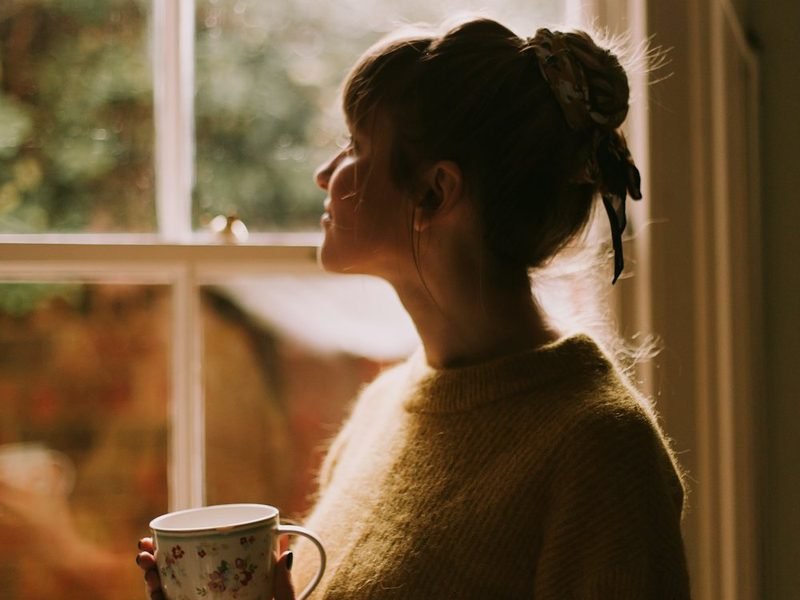 A woman holding a cup of tea, looking out of a window