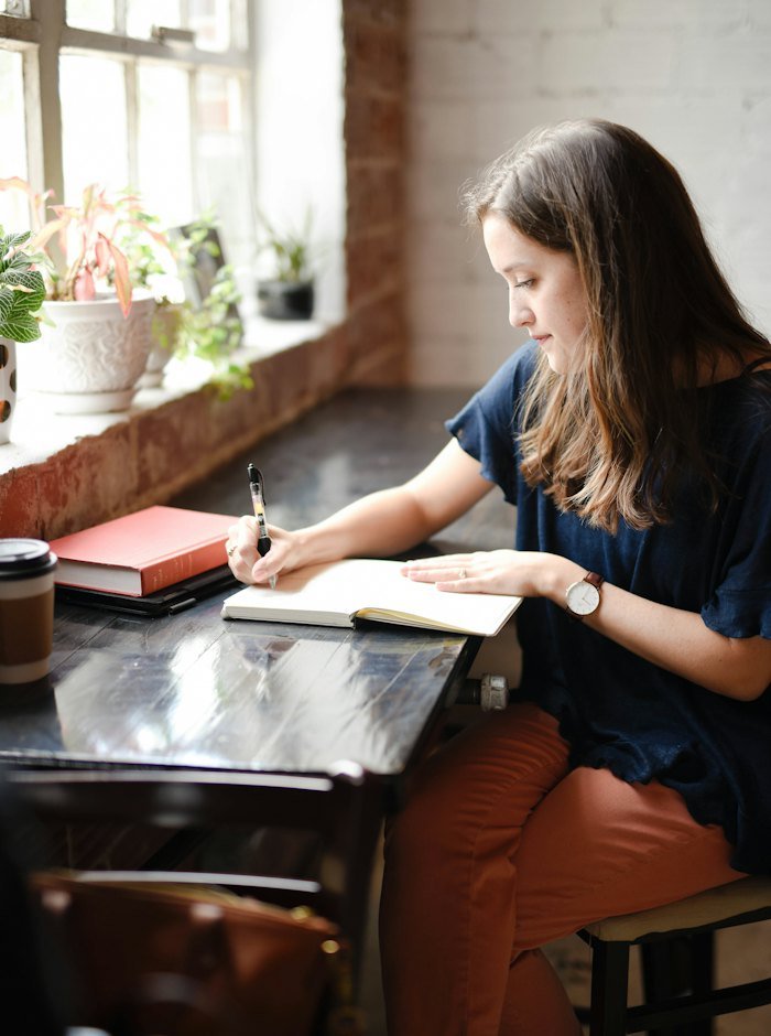 A young woman writing in her journal by a sunny window