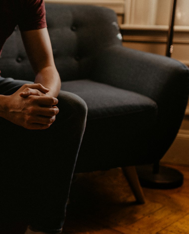 A young man sitting in an armchair with his hands clasped, ready to talk