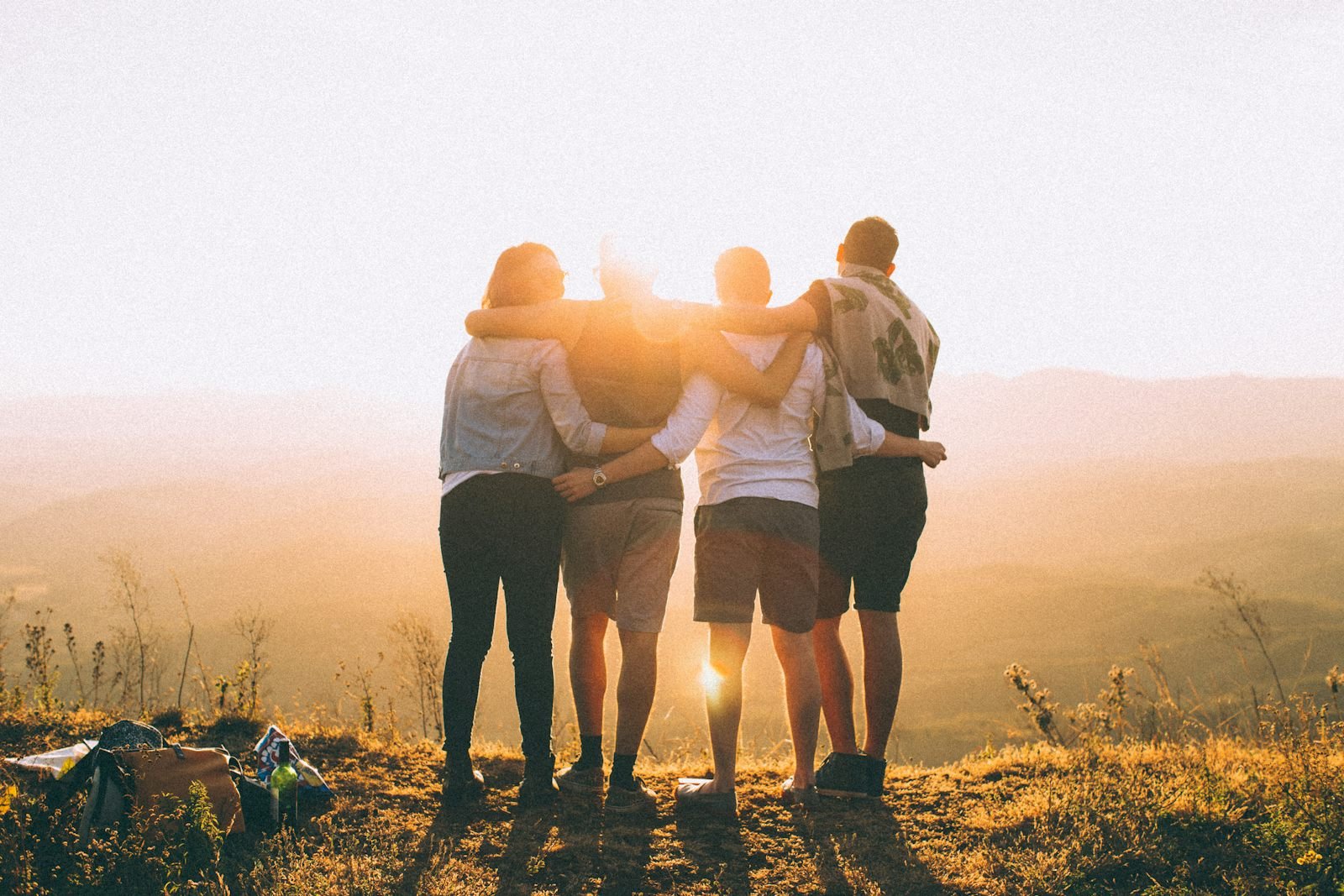 Four friends standing arm in arm on a hilltop, looking out at the sunrise