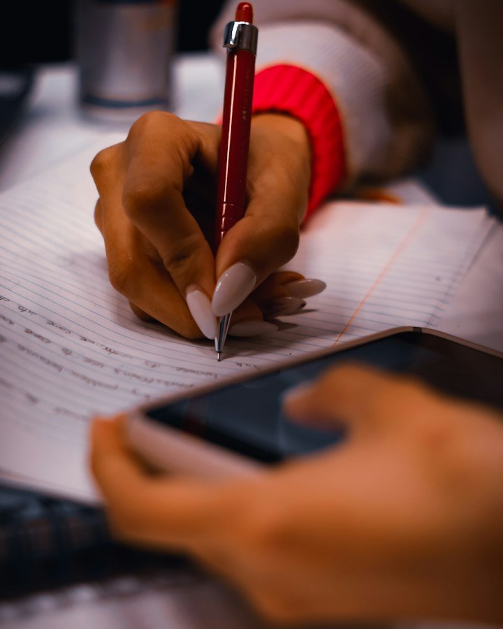 A person writing answers on paper beside a phone
